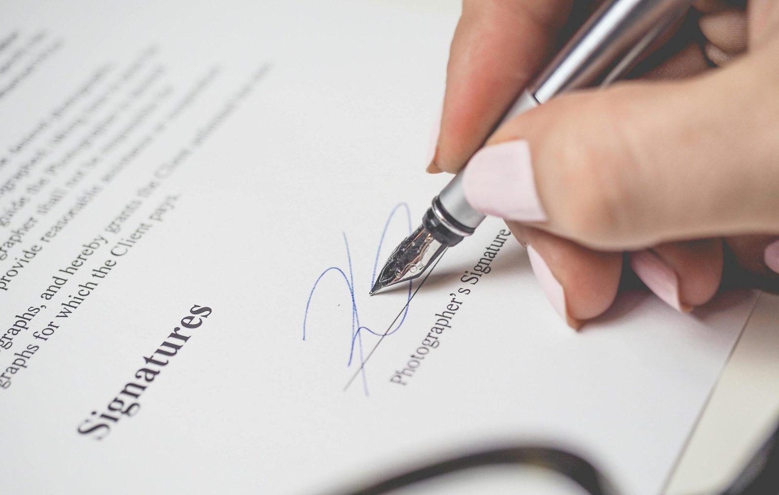 Close-up of a hand signing a contract, showcasing a pen and elegant handwriting.